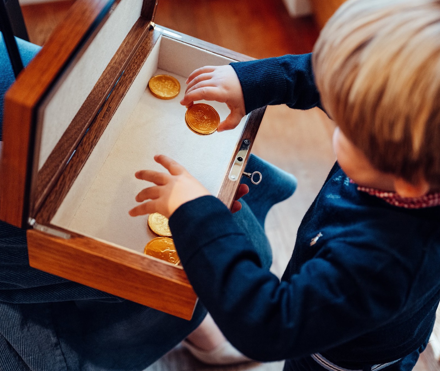A young boy playing with gold coins inside a box.