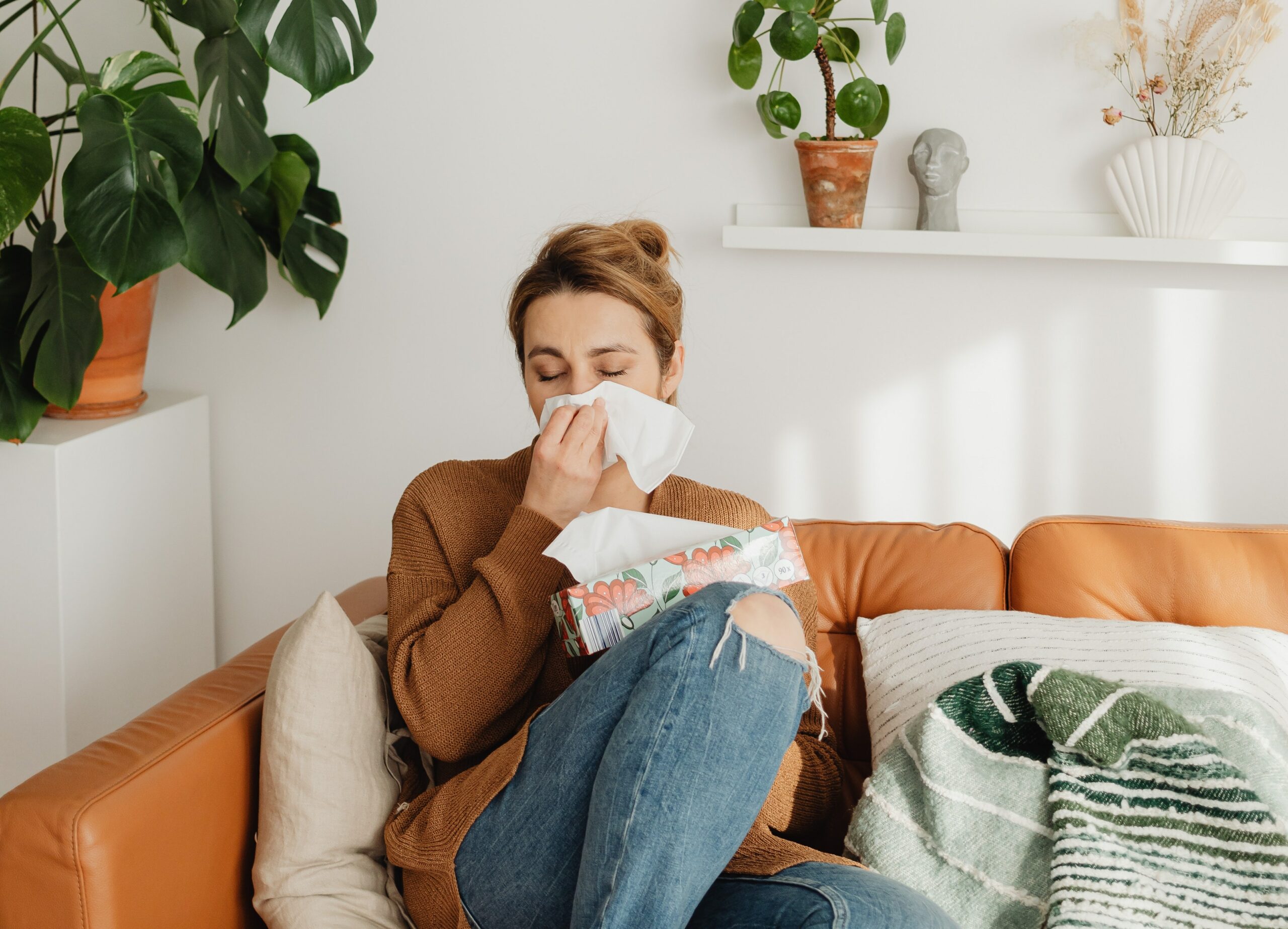 A woman sat on a sofa, blowing her nose as she's got Hay Fever.